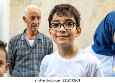 Bethlehem, West Bank, Palestine - 22 July 2022: Young Arab Boy With Brown Hair In White Shirt And Black Glasses Smiles With Old Man And Woman With Hijab In The Background