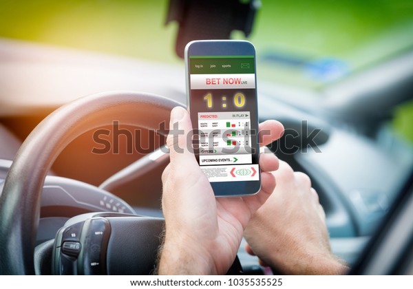Betting on sports,\
holding smart phone with working online betting mobile application\
while driving a car