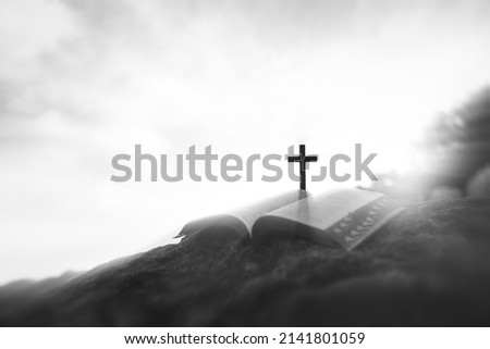 Between the bright sky and clouds, the cross of suffering of Jesus Christ symbolizing sacrifice and resurrection, and the holy bible on the hill

