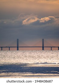 Öresundsbron Between Sweden And Denmark, Seen In The Distance From Lomma Beach Under Dramatic Sunset Light And Cloudes, Over Wavy Seas. 