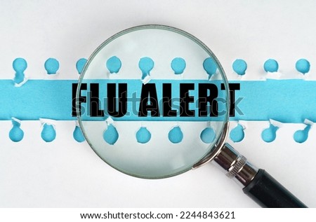 Between two sheets from a notebook on a blue stripe with the inscription - Flu alert, there is a magnifying glass. Medical concept.