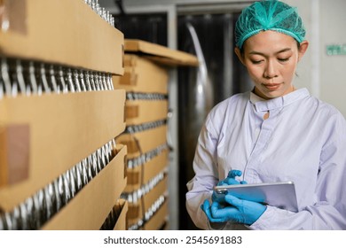 At a beverage factory a woman in QC uses a digital tablet to inspect products on the conveyor belt. She manages quality control while examining the bottling line for liquid manufacturing. - Powered by Shutterstock