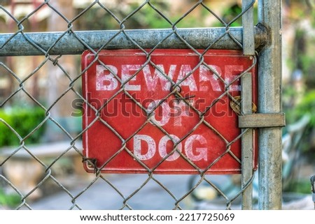 Beware of dog sign on a chain link fence in the suburbs of San Antonio Texas. CLose up view of an old and weathered red sugnage warning people to be cautious of dogs.