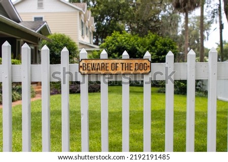 Beware of the dog sign posted on white fence outside a house yard
