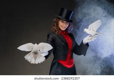 A bewitching moment captured as a woman magician in a magician's costume and black cylinder hat showcases enchanting magic tricks with graceful white doves on a dark, smoky backdrop