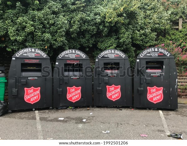 Bexhill -Sussex-U.K. -\
June 17 ,2021: Four black recycling bins for clothes and shoes\
stand in line in a car park . Salvation Army Charity collection\
point and drop off .