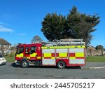 Bexhill-East Sussex-UK-April 3, 2024: Side view of a fire engine parked in a residential street with housing and trees in background.Emergency Services.