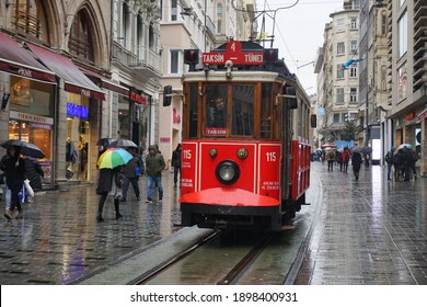 Beyoglu, Istanbul, Turkey, 05.12.2018, Red Retro Tramway On Taksim Istiklal Street In A Rainy Day. People Are Walking With Umbrellas From The Sides Of The Tramway.