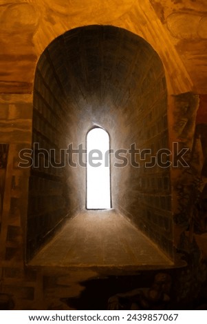 Beyond the Breach. Looking out into blinding sunlight, the narrow window of an old cathedral castle seems a passage to another world.  Inside is dark, gloomy, and drab on the stone walls