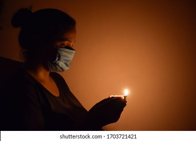 Bharuch, Gujarat / India - April 5 2020: Covid 19 Corona Virus, A Girl In Mask Lighten Up Lamp And Diya To Show Together We Stand To Fight Corona Virus. Selective Focus On Girl And Black Background.