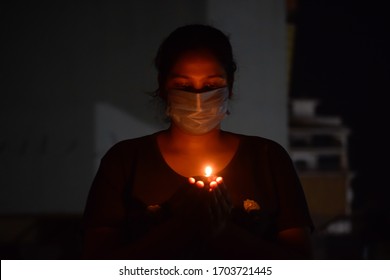 Bharuch, Gujarat / India - April 5 2020: Covid 19 Corona Virus, A Girl In Mask Lighten Up Lamp And Diya To Show Together We Stand To Fight Corona Virus. Selective Focus On Girl And Black Background.