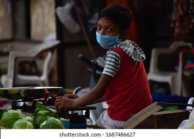 Bharuch, Gujarat / India - March 20, 2020: An Indian Boy Child Wearing MEDICAL MASK For Protection, Safety, Prevention Of COVID 19 CORONA VIRUS Selling Vegetables Fruit In Market Crowd In Lockdown.