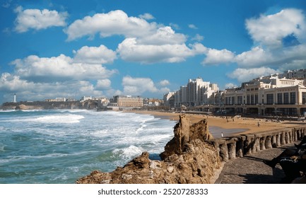 A Biarritz beach with a rocky shoreline and a pier. The sky is cloudy and the water is choppy - Powered by Shutterstock