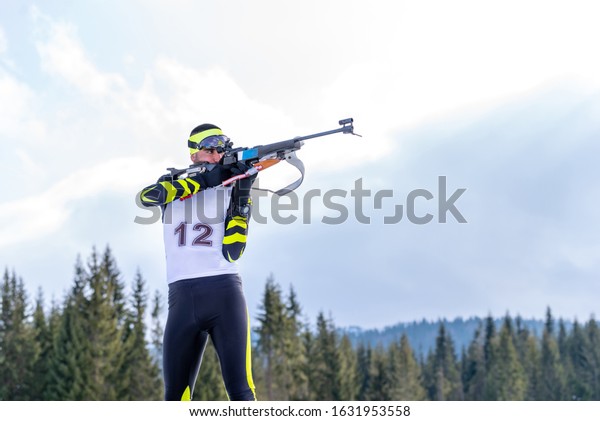 Biathlete holds his breath while\
shooting the rifle in a standing position during the biathlon\
race