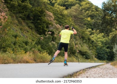Biathlon workout. Athletic man training on the roller ski at country road, back view. Concept of competition and summer activity.