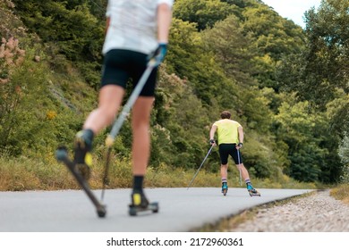 Biathlon workout. Two athletic men training on the roller ski at country road, back view. Low angle view. Concept of sports competition and summer activity.