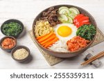 Bibimbap is a Korean dish in the form of a bowl of white rice topped with side dishes of vegetables, beef, eggs and spicy gochujang sauce.