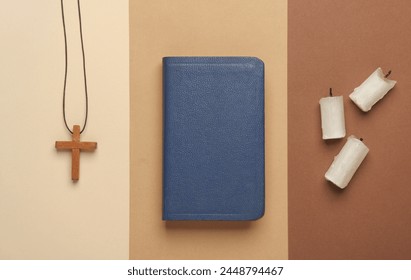 Bible book, candles and wooden Christian cross on a string, beige background. Religion, prayer, going to church concept. Top view. Flat l;ay