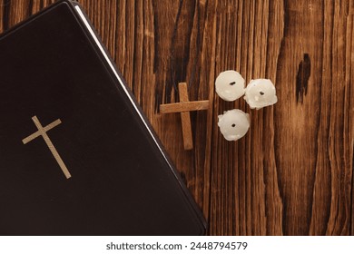 Bible book, candles and wooden Christian cross on a string, wooden table. Religion, prayer, going to church concept