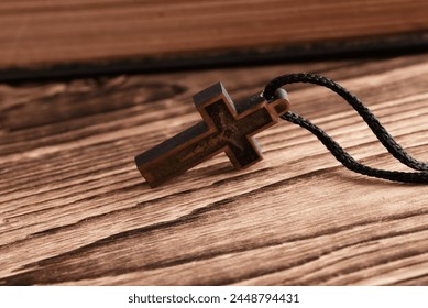 Bible book and wooden Christian cross on a string, wooden table