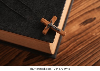 Bible book and wooden Christian cross on a string, wooden table