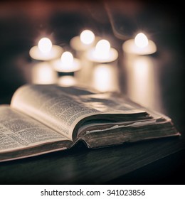 Bible With Candles In The Background. Low Light Scene.