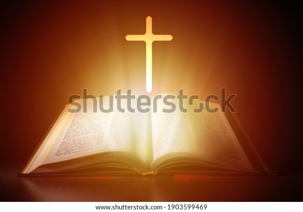 Bible\
and cross on a dark background. Bright light comes from Christian\
Bible. Cross next to the open book. Bible study concept. Studying\
Christian religion Reading religious\
literature.