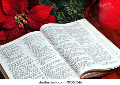 Bible Open To The Nativity Story In Luke With Poinsettia, Evergreen, And Candle