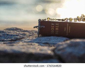 Bible and Rosary Necklace on stone with morning light reflex on sea water as background.Faith in God. Pray for you.Believe in goddess. Love study bible. Holy book,Christianity background concept.