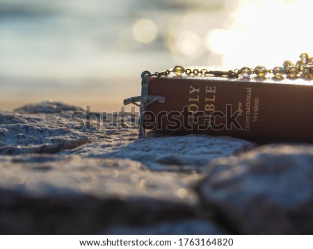 Bible and Rosary Necklace on stone with morning light reflex on sea water as background.Faith in God. Pray for you.Believe in goddess. Love study bible. Holy book,Christianity background concept.