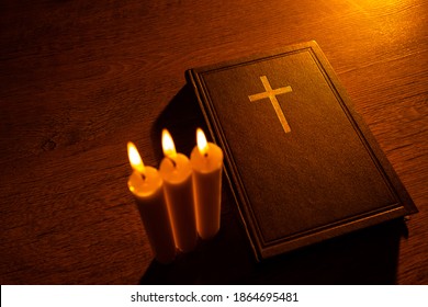 A Bible and three burning candles on a wooden table. Christian sermon. Christian faith. Protestantism, Catholicism and Orthodoxy. Faith in Jesus Christ. Study of the word of God.