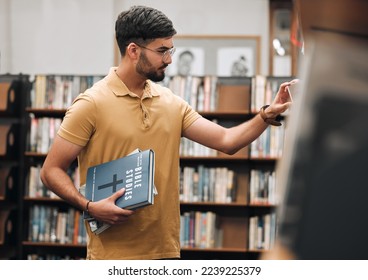 Bible, university or student in a library to research spiritual religion knowledge, prayer or Christianity by bookshelf. Nerd, school, focused young man in college studying or learning faith in God - Shutterstock ID 2239225379