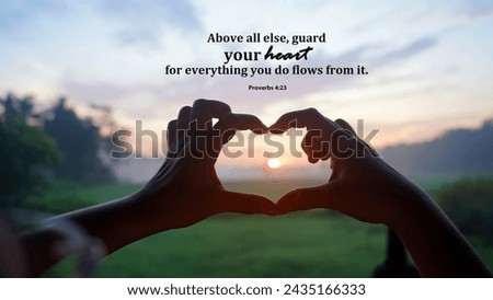 Bible verse quote from Proverbs 24:3 - Above all else, guard your heart for everything you do flows from it. With hands of a woman making love sign. Person showing heart shape against the sun.