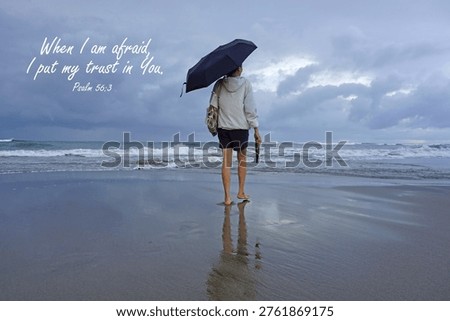 Bible verse quote - When i am afraid, i put my trust in You. Psalm 56:3 On beach background with a woman holding black umbrella walking on sand in the beach on a cloudy day. Religious words, Christianity faith concept.