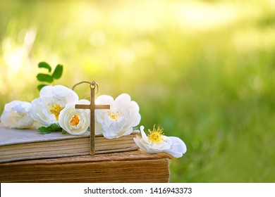 biblical old books, Christian cross and flowers on sunny green natural background. concept of religion, faith in God, Church, Easter holiday, Ascension Day. copy space