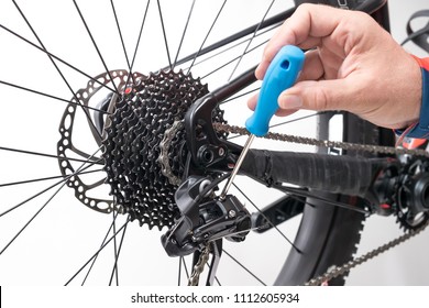 Bicicle repair or maintenance. Adjustment of rear deraileur or gear changer with a blue screwdriver. Setting minimum or maximum adjustment on a modern mountain bicycle.