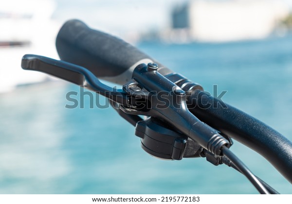 Bicycle brake lever. Bicycle brake\
lever and grip, close-up, plastic, black, brake cable, blurred\
background, with sea background, diagonal angle,\
handle