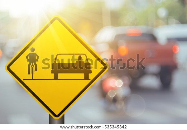 Bicycle and\
car share warning sign on blur traffic road with colorful bokeh\
light abstract background. Copy space of transportation and travel\
concept. Vintage tone filter color style.\
