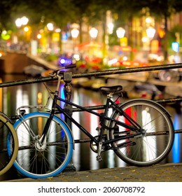 Bicycle and evening street lights. Quiet scene at night in Amsterdam. Lots of lights, a canal, an old bridge and a bike. Selective focus. Amsterdam, Holland, Europe