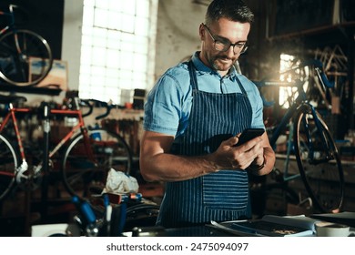 Bicycle, garage and phone for man, reading and small business of mechanic, apron and equipment. Proud, owner and person with service, maintenance and tools for bike, technician or working with mobile - Powered by Shutterstock