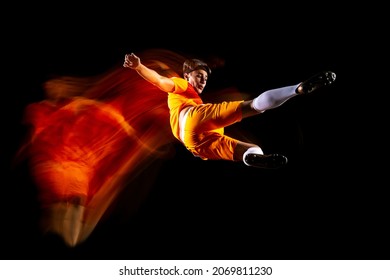 Bicycle kick. Portrait of young male soccer football player in unifom in action. Man training isolated over black background. Concept of action, team sport game, energy. Copy space for ad
