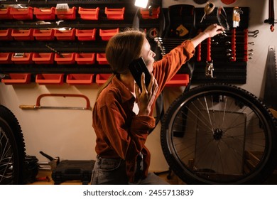 Bicycle maintenance and repair concept. Young blonde woman working in garage calling on mobile phone consulting with mechanic. Copy space - Powered by Shutterstock