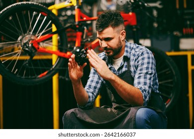 Bicycle mechanic carefully examining a bike part, possibly a gear or brake component, while working in a professional workshop