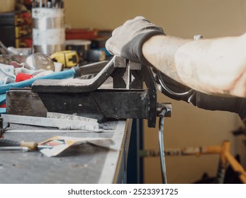 Bicycle mechanic wearing gloves is using a bench vise to hold a piece of metal while he works on a bicycle frame in his repair shop - Powered by Shutterstock