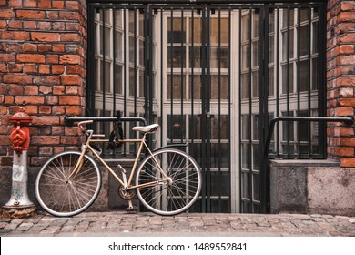 Bicycle next to the fire hydrant leaned on the wall of the grating old red brick building. The streets on Copenhagen in Denmark. Focused on building.
