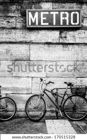 Bicycle parked against a stone block wall under a French metro subway sign. Black and white image. Copy space.