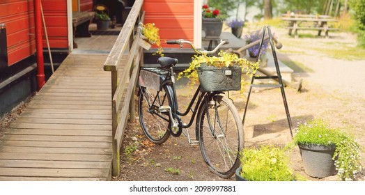 Bicycle Parked Near Modern Traditional Country House Colored With Falu Red Dye. Summer Garden, Green Trees, Flowers, Exterior Decor. Stockholm Sail Club, Mälaren Lake, Sweden. Estate, Architecture