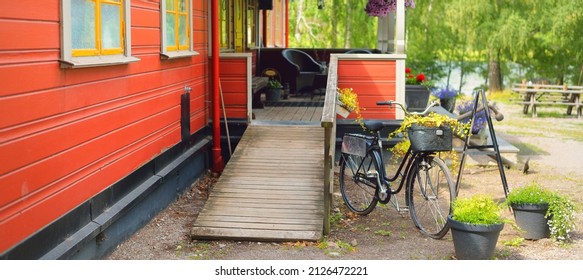 Bicycle Parked Near Modern Traditional Country House Colored With Falu Red Dye. Summer Garden, Green Trees, Flowers, Exterior Decor. Stockholm Sail Club, Mälaren Lake, Sweden. Estate, Architecture