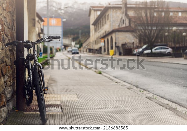 Bicycle parked on sidewalk near city street in\
Spain. Bike lean on pole beside old building. Front view of bicycle\
on blurred building, car driving on the road, and mountain\
background. Europe\
travel.
