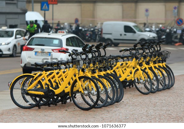 Bicycle rent at the street with many same\
yellow bikes stand in a row in Milan,\
Italy